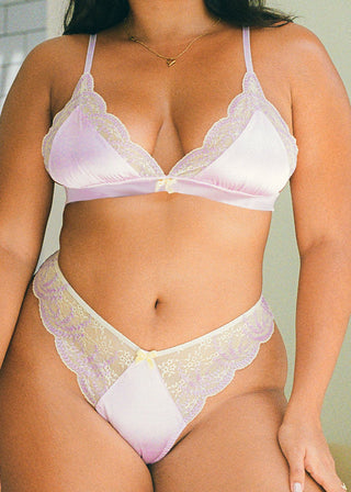 Woman wears a lilac satin thong with yellow lace details at the sides. The elegant thong features a v-shape form and a bow detail. This elegant lingerie is from Lioa Lingerie, a Swiss Lingerie Brand.