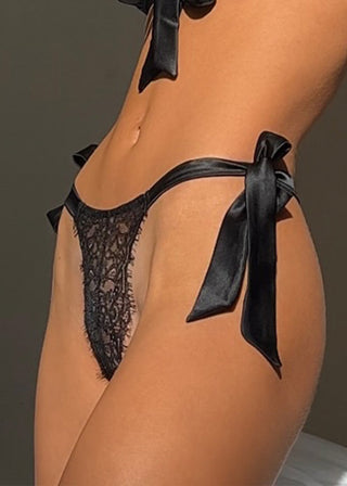 Woman wears a black lace thong with big satin bows to tie at the sides. The black thong is from Lioa Lingerie, a Swiss Lingerie Brand, made in Portugal.