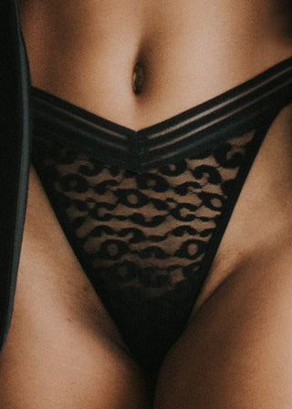 Woman wears a black thong with a v-shape and leopard print. The classic thong features a stripe band and a figure-flattering fit and is from Lioa Lingerie, a Swiss Swimwear Brand.