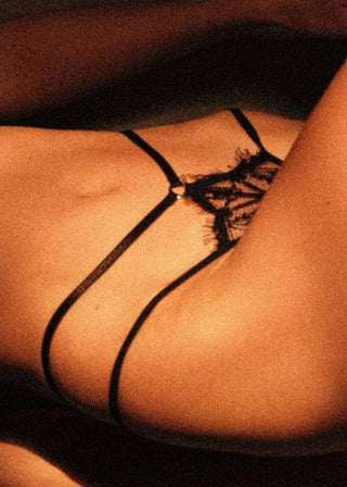 Woman wears classic black thong with strap details, delicate lace and a golden ring detail and is from Lioa Lingerie, a Swiss Lingerie Brand.