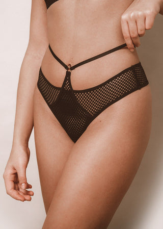 Woman wears a black thong with a golden ring detail and strap around the waist. The black lingerie features a sexy net mesh and is from Lioa Lingerie, a Swiss Lingerie Brand.