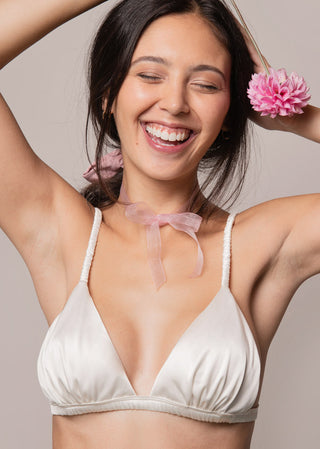 Woman wears a classic triangle bra in satin. This cups of this satin bralette are slightly ruffled and look cute. The white lingerie is from Lioa Lingerie, a Swiss Lingerie Brand.