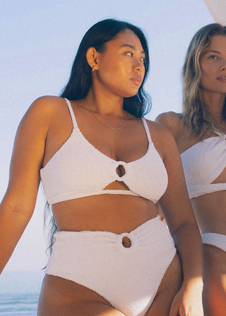 Woman wears sporty bikini top in white with textured fabric. The supportive bikini has a ring detail and cut out in the front. It’s a sustainable bikini from Lioa Lingerie, a Swiss Swimwear Brand.