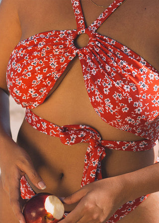 Woman wears a red bikini top with a ring detail at the front and multiple options to wear. The sustainable bikini features a floral print on red and is from Lioa Lingerie, a Swiss Swimwear Brand.