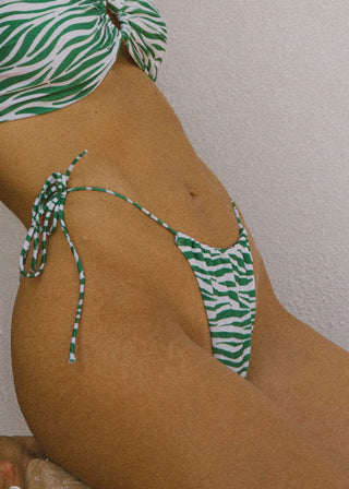Woman wears cheeky bikini bottoms with tieable side straps and a zebra print. This sustainable zebra bikini bottom is from Lioa Lingerie, a Swiss Swimwear Brand.