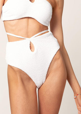Woman wears a high-waist bikini with textured fabric. The white bikini bottom has a cut out and straps to tie around the waist and is from Lioa Lingerie, a Swiss Swimwear Brand.