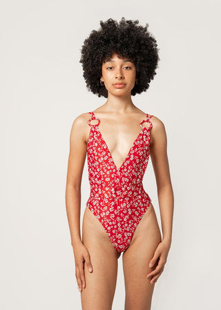 Woman wears red swimsuit with floral print and a belt. The luxurious swimsuit features two big ring details at the front. This sustainable swimwear is from Lioa Lingerie, a Swiss Swimwear Brand.