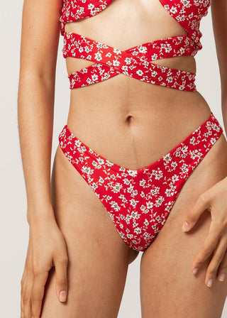 Woman wears cheeky bikini bottom in red with floral details and a classic v-shape. The figure-flattering bikini bottom is a sustainable swimwear piece and from Lioa Lingerie, a Swiss Swimwear Brand.