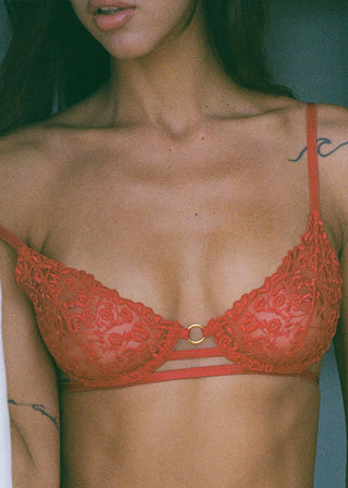 Woman wears elegant red bralette with embroidery, golden ring and strap details.